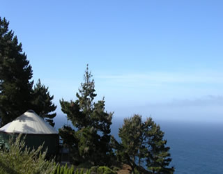 Picture of a yurt snuggled in trees overlooking the coast